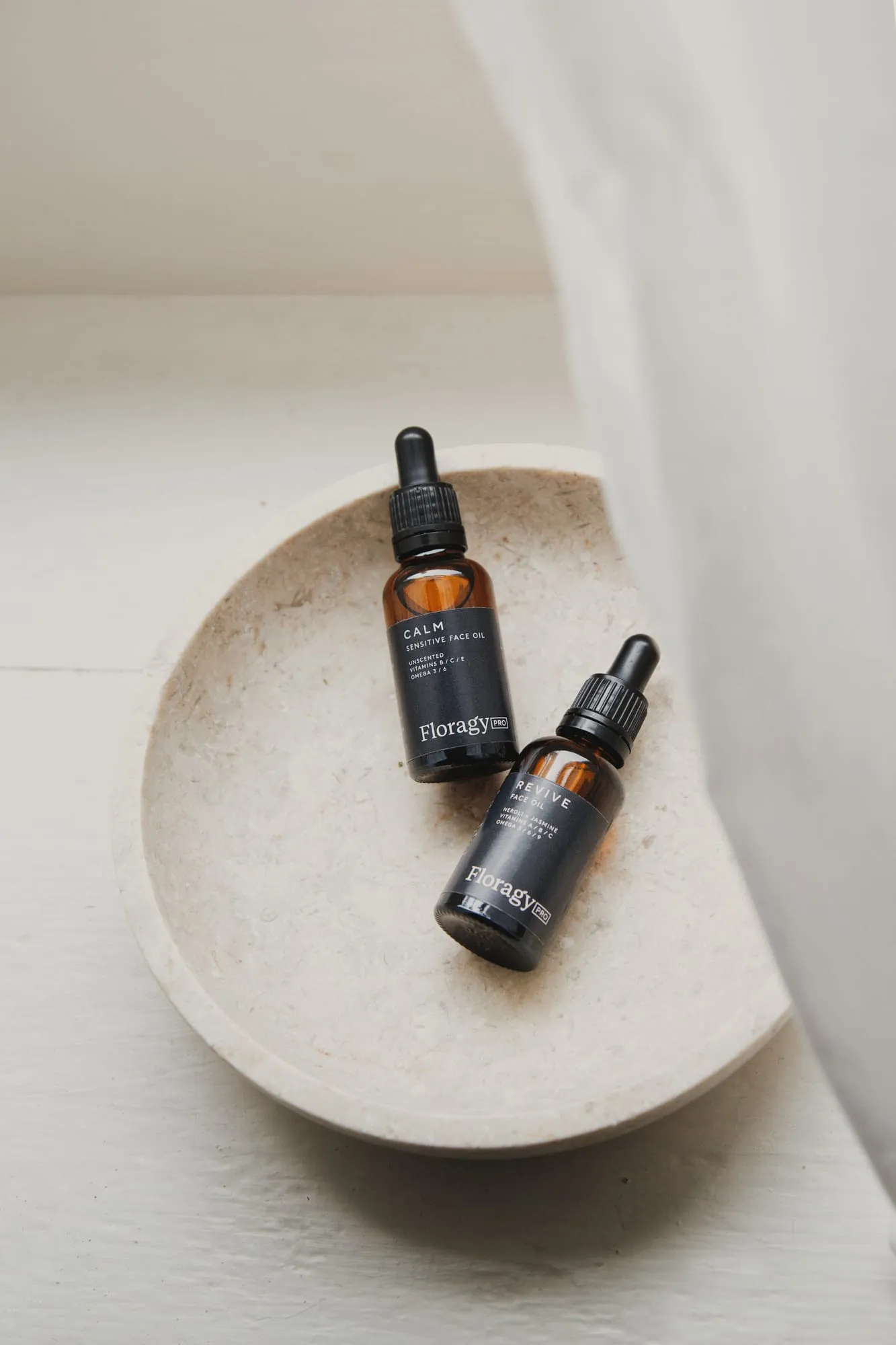 Two Floragy Pro botanical face oils resting in a stone dish